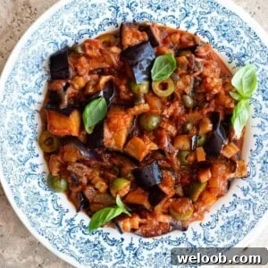 A close up of Sicilian eggplant caponata in a blue and white bowl with basil on top.