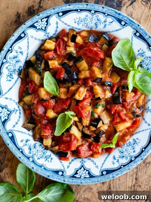 Fried eggplant in tomato sauce with fresh basil in a blue and white bowl on a wooden surface.
