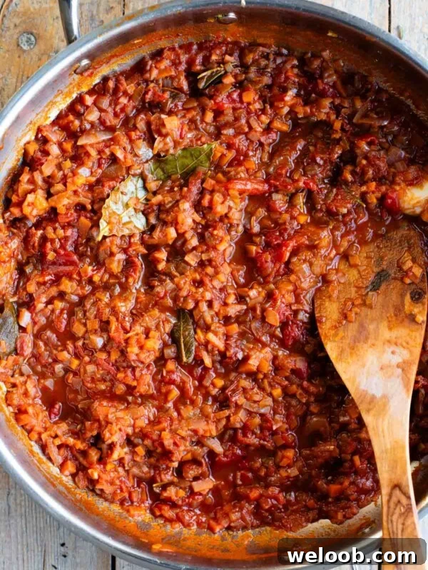 An overhead shot of a skillet with an Italian slow cooked vegetable sauce sitting on a wooden table.