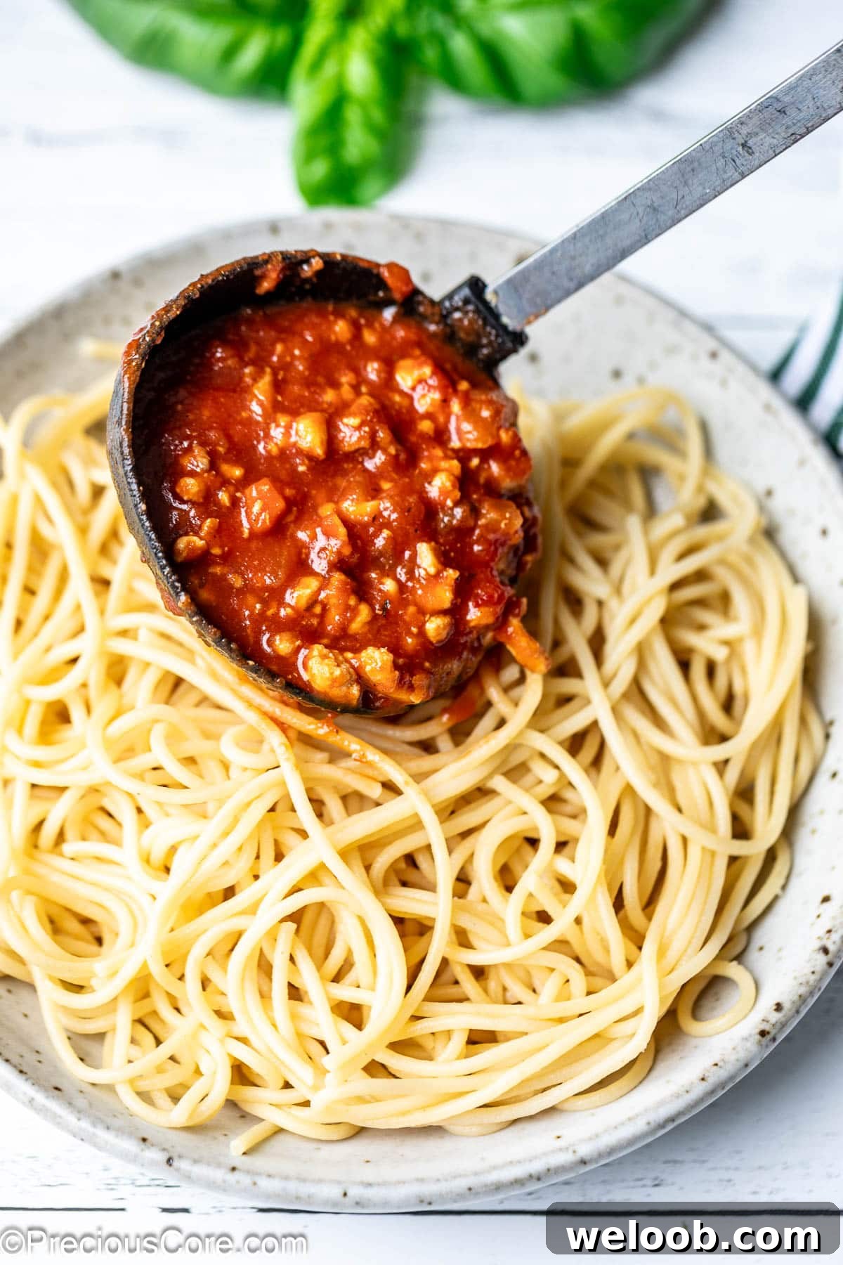 Pouring red meaty sauce over cooked spaghetti.