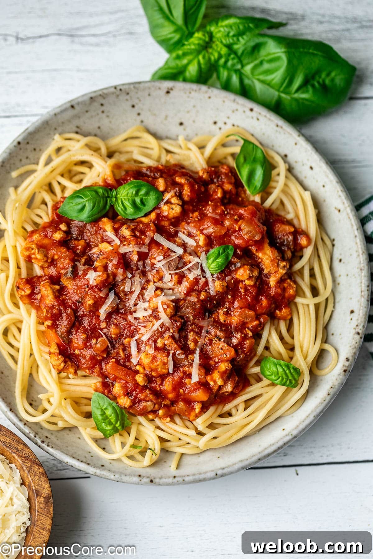 A bowl of spaghetti topped with red sauce, parmesan, and basil leaves.