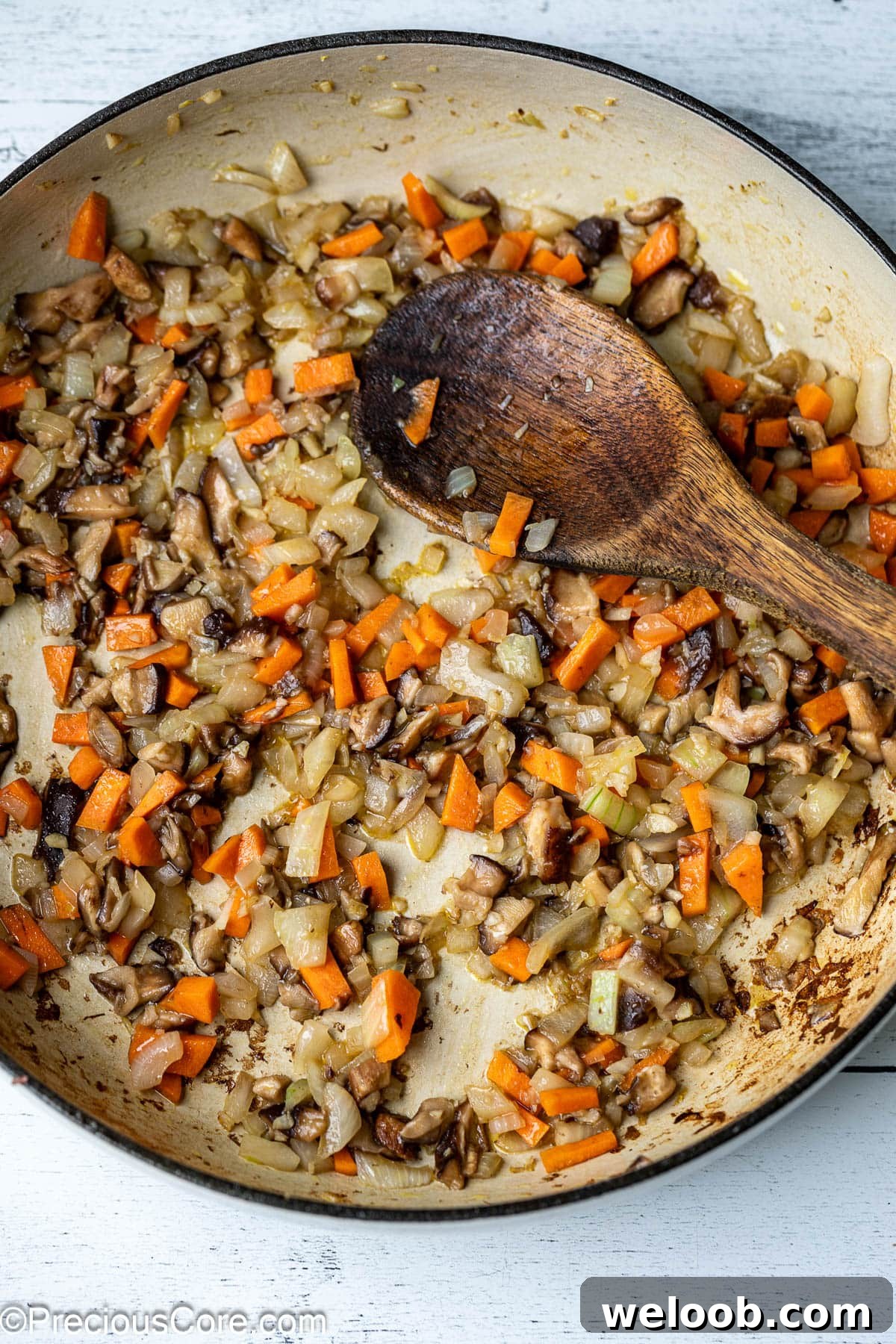 Sautéed onions, carrots and mushrooms in a pot.