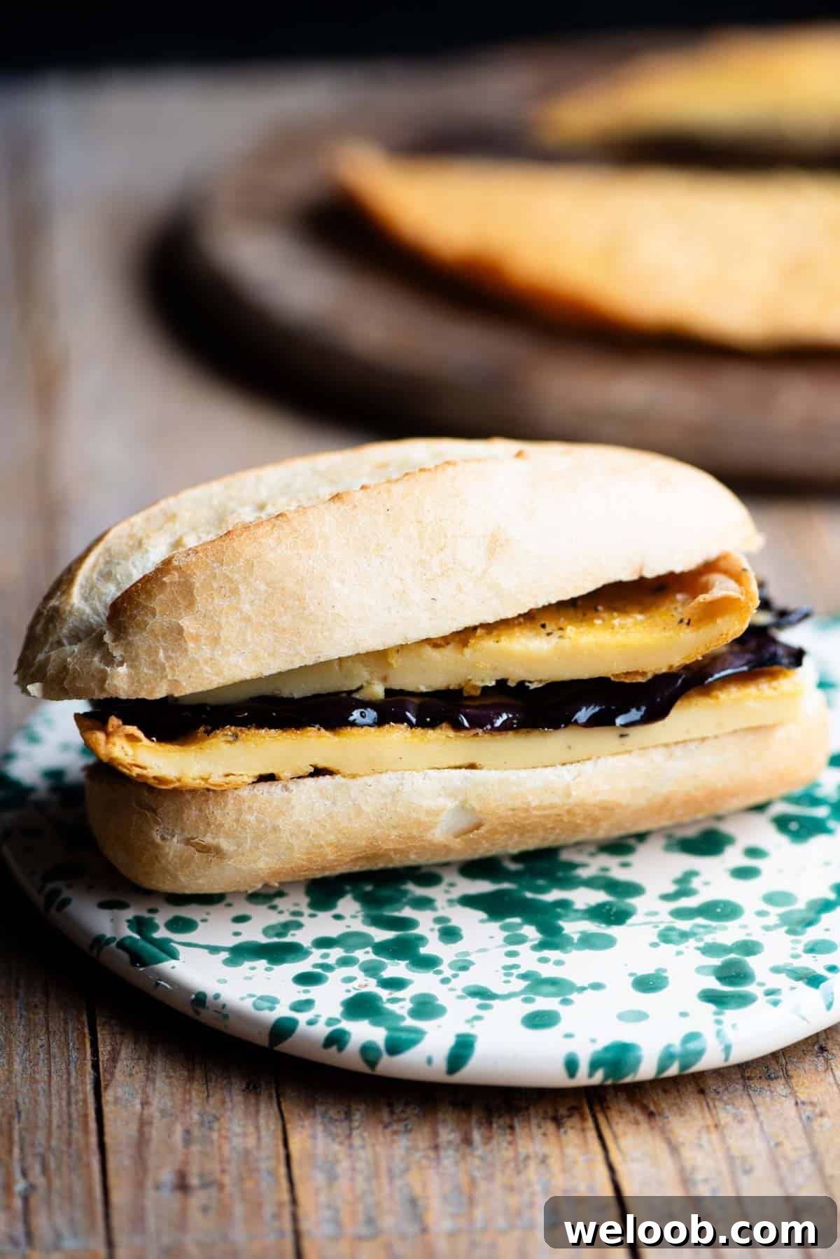 A cinque e cinque Livornese sandwich on a rustic wooden surface. The crusty roll is filled with chickpea farinata and marinated eggplant.