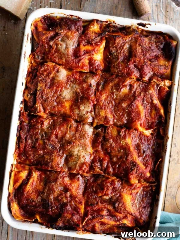 An overhead shot of a Neapolitan lasagna sitting on a wooden table with a bottle of wine at the side.
