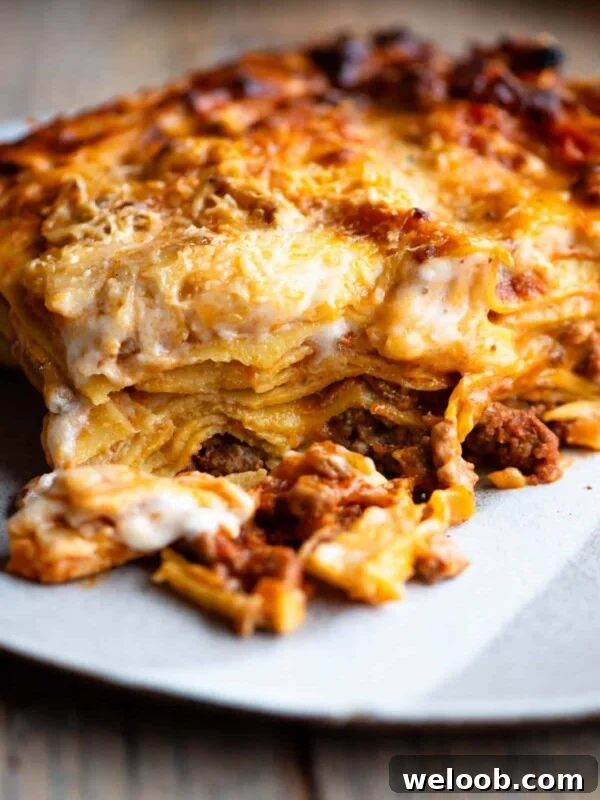 One slice of lamb lasagna on a plate sitting on a wooden surface.