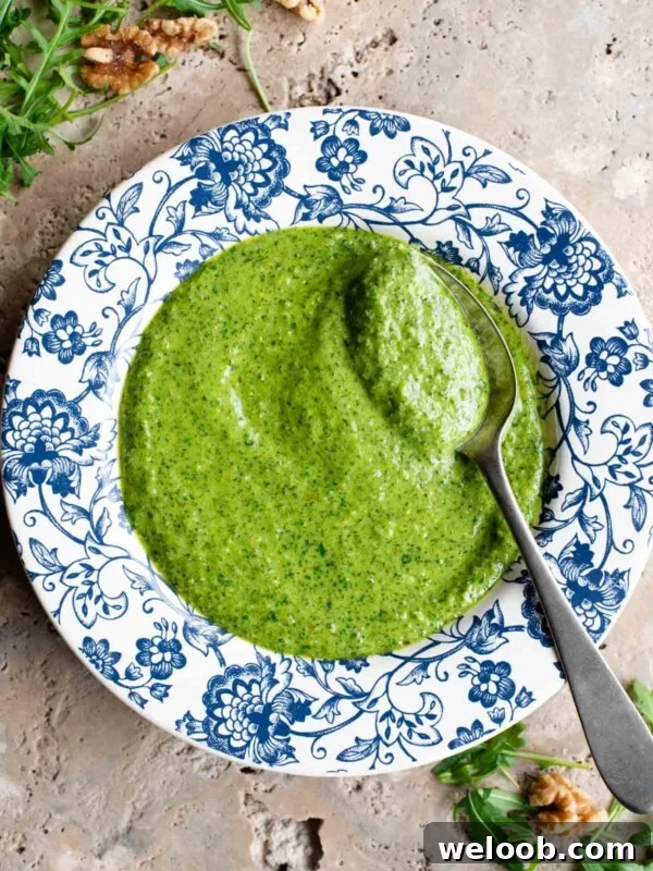 An overhead shot of arugula pesto in a blue and white patterned bowl with a spoon at the side.