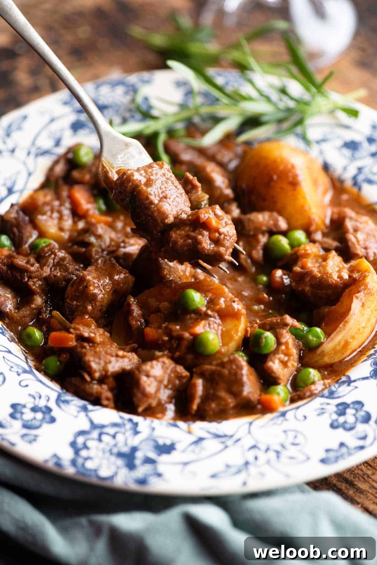 A close up of a fork picking up some beef from a bowl of beef stew.