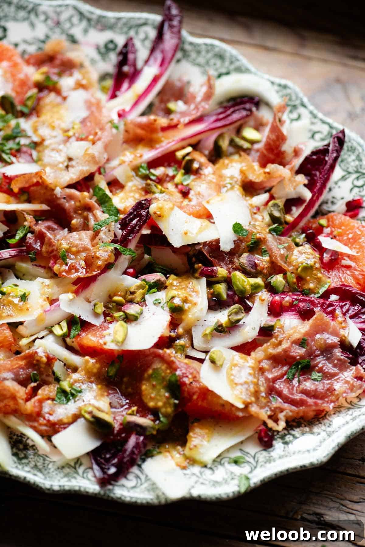 A side shot of a festive salad with blood orange, raddichio, prosciutto, pecorino, pomegranate and pistachios.