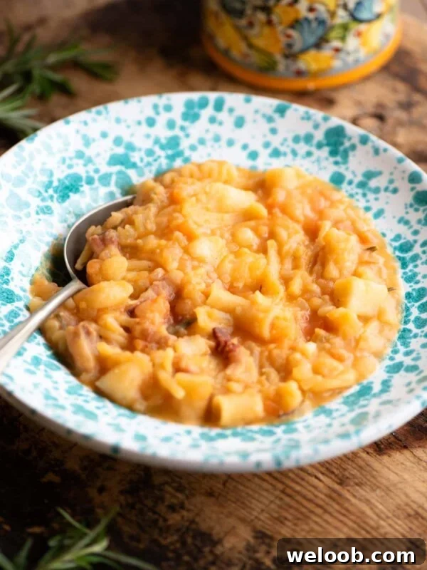 Pasta e Patate (potatoes) in a blue speckled bowl with a spoon sitting on a wooden surface.