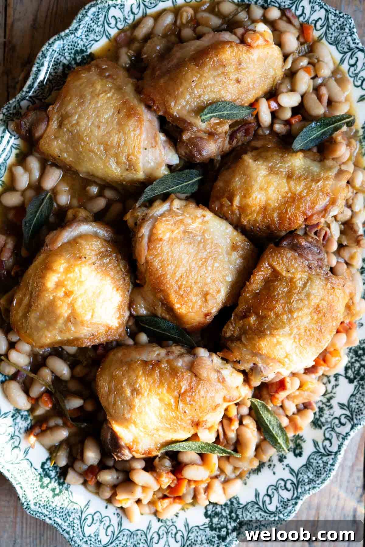 Italian braised chicken thighs on a bed of cannellini beans and vegetables served on a green vintage style serving plate.