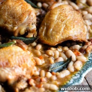 Braised Chicken with Pancetta, White Beans and Fresh Sage 11 A close up of braised chicken thighs sitting on a plate with beans in sauce with sage and vegetables.
