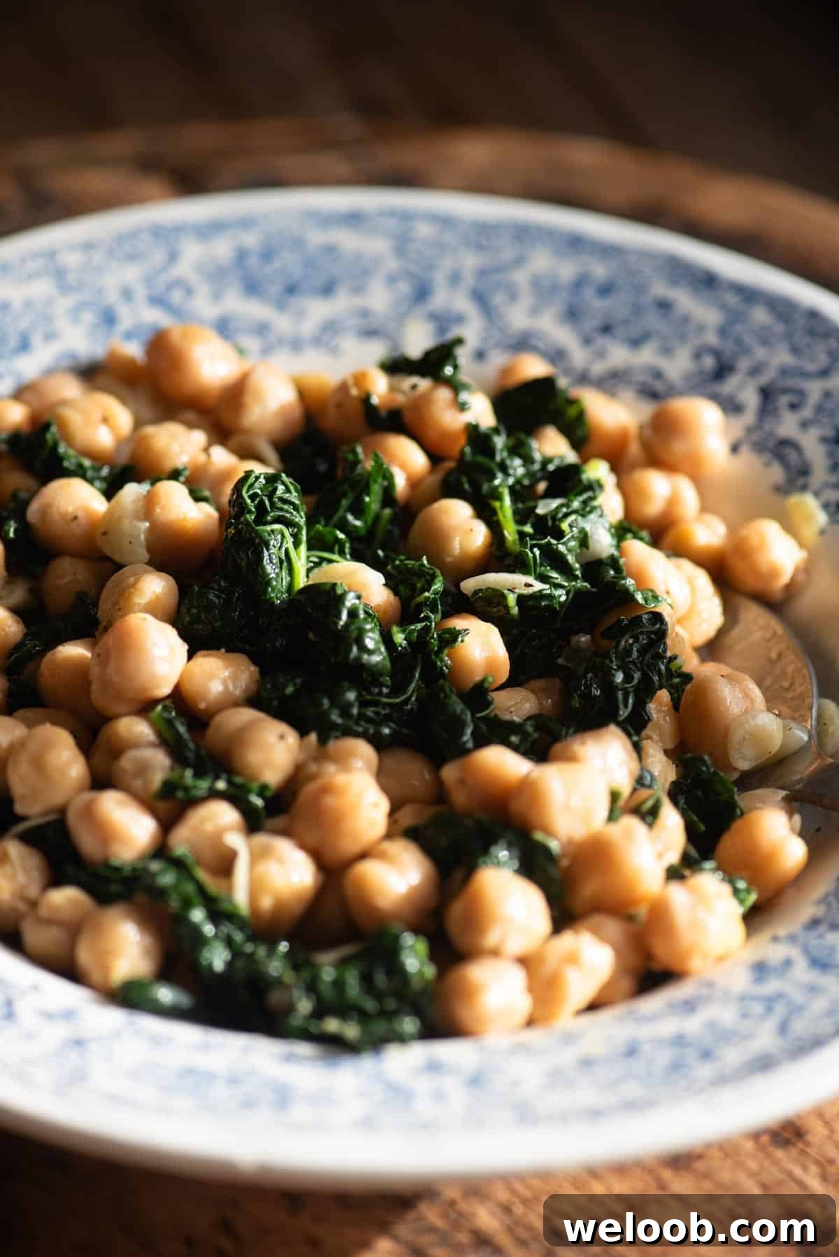 A close up of chickpeas and cavolo nero in a blue and white vintage style bowl sitting on a rustic wooden surface.