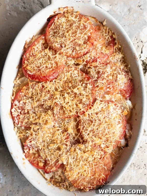 An overhead shot of an Italian potato and tomato gratin in an oval dish sitting on a Travertine background.