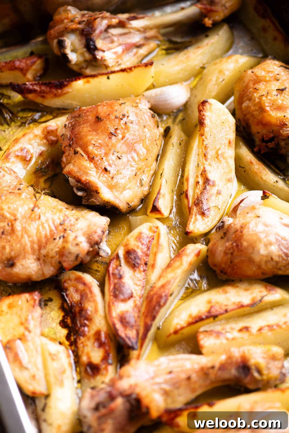 A close up side shot of roasted chicken thighs and drumsticks with potato wedges in a roasting tray.