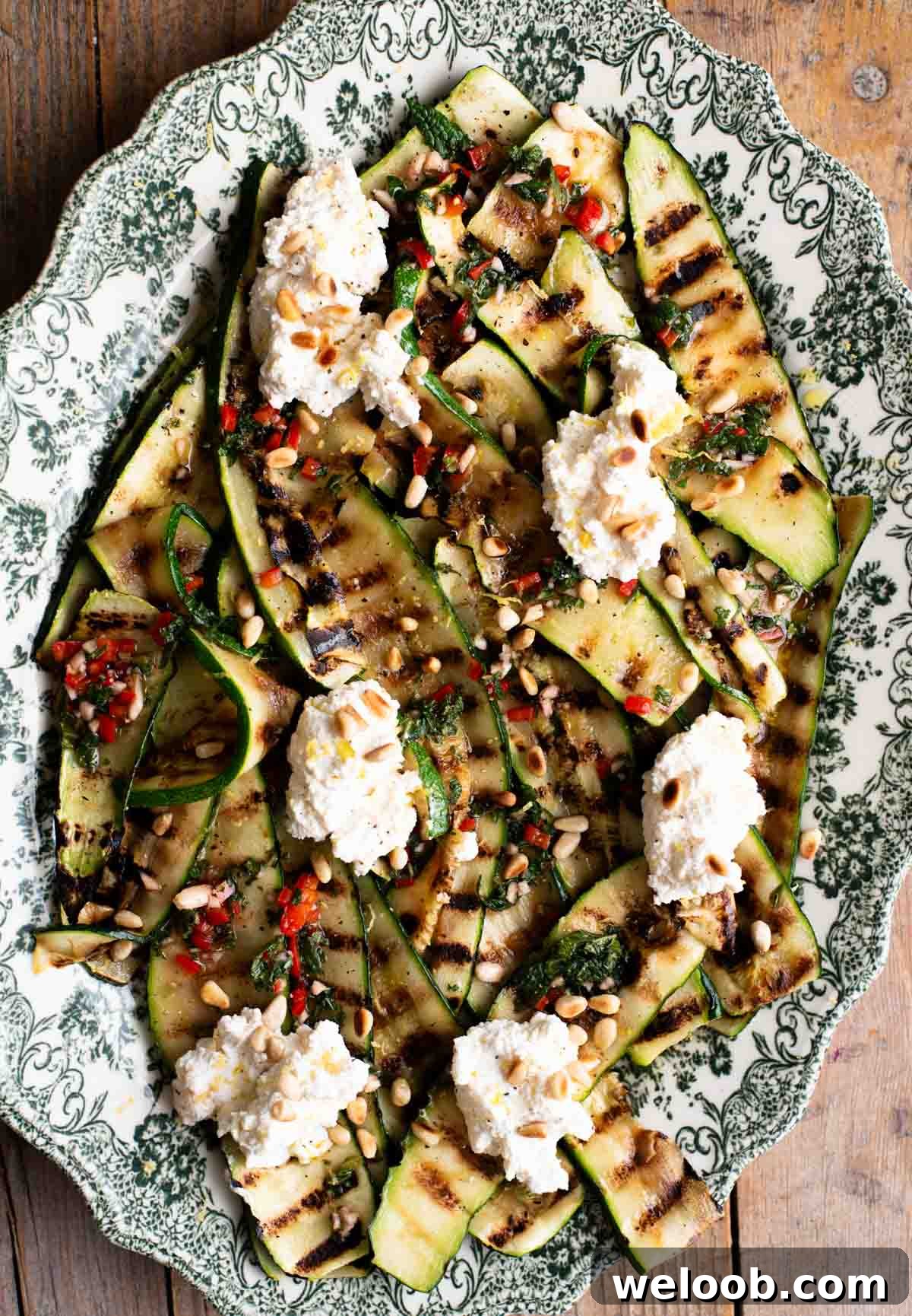An overhead shot of grilled zucchini on a serving platter topped with garlic, chilli, mint and ricotta.