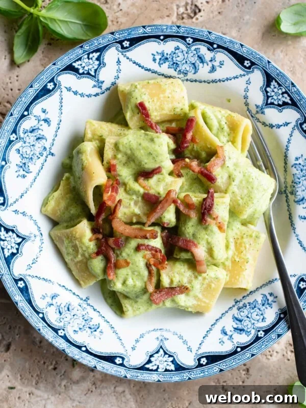 A creamy zucchini pasta in a blue and white bowl topped with crispy pancetta sitting on a travertine surface.