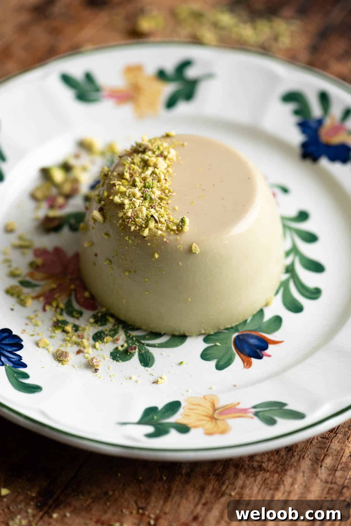 A pistachio panna cotta on a vintage floral plate topped with crumbed pistachios.