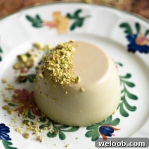 A close up of a pistachio panna cotta on a floral plate garnished with chopped pistachios.