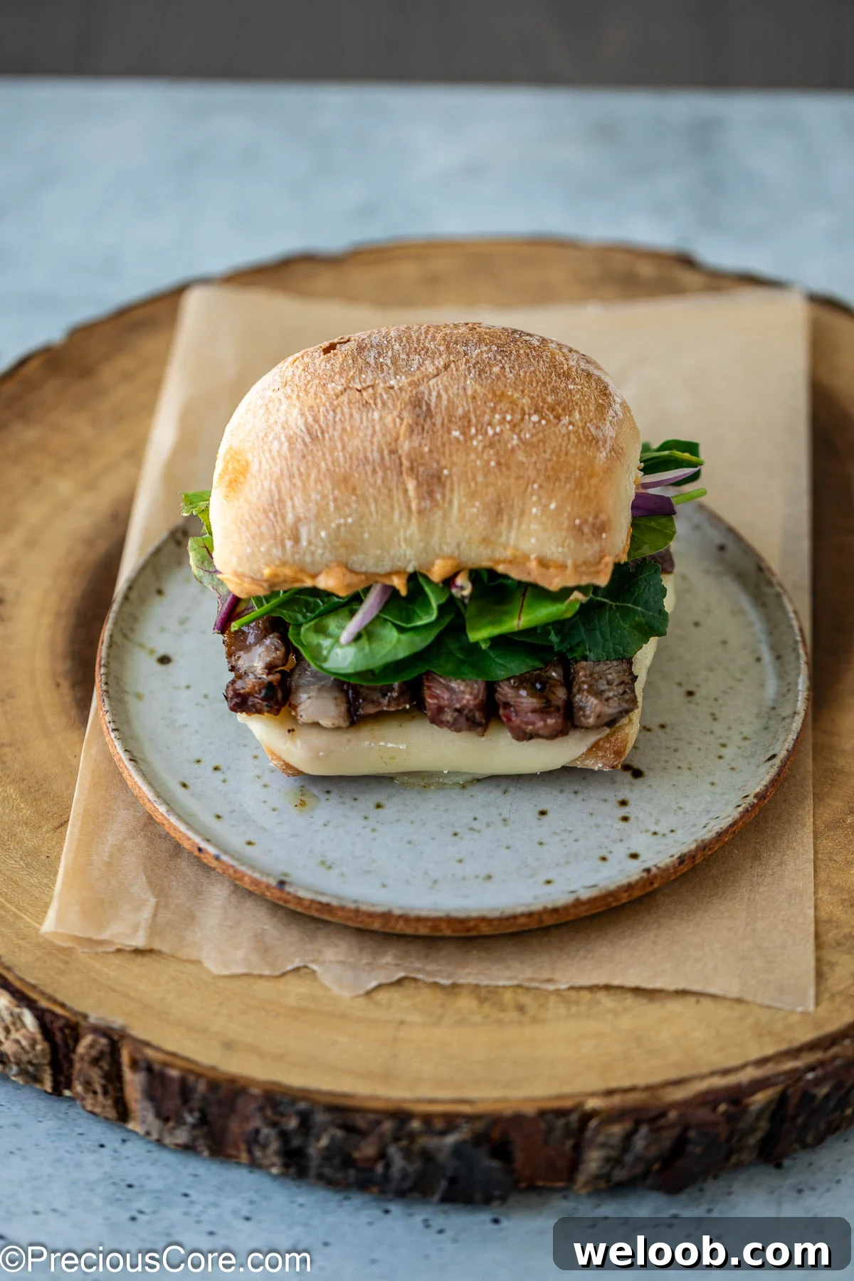 Assembled sandwich with ribeye steak, greens, onions, and cheese.