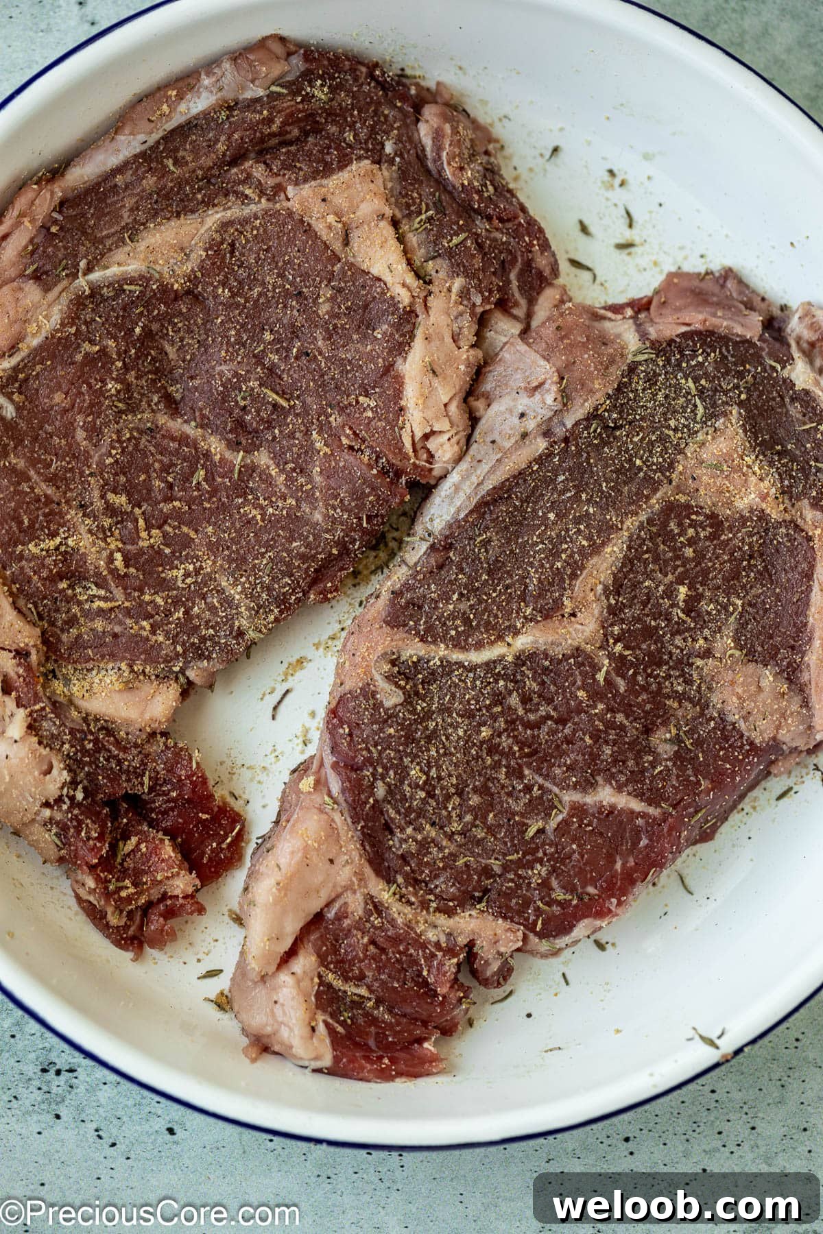 Seasoned raw ribeye steaks.