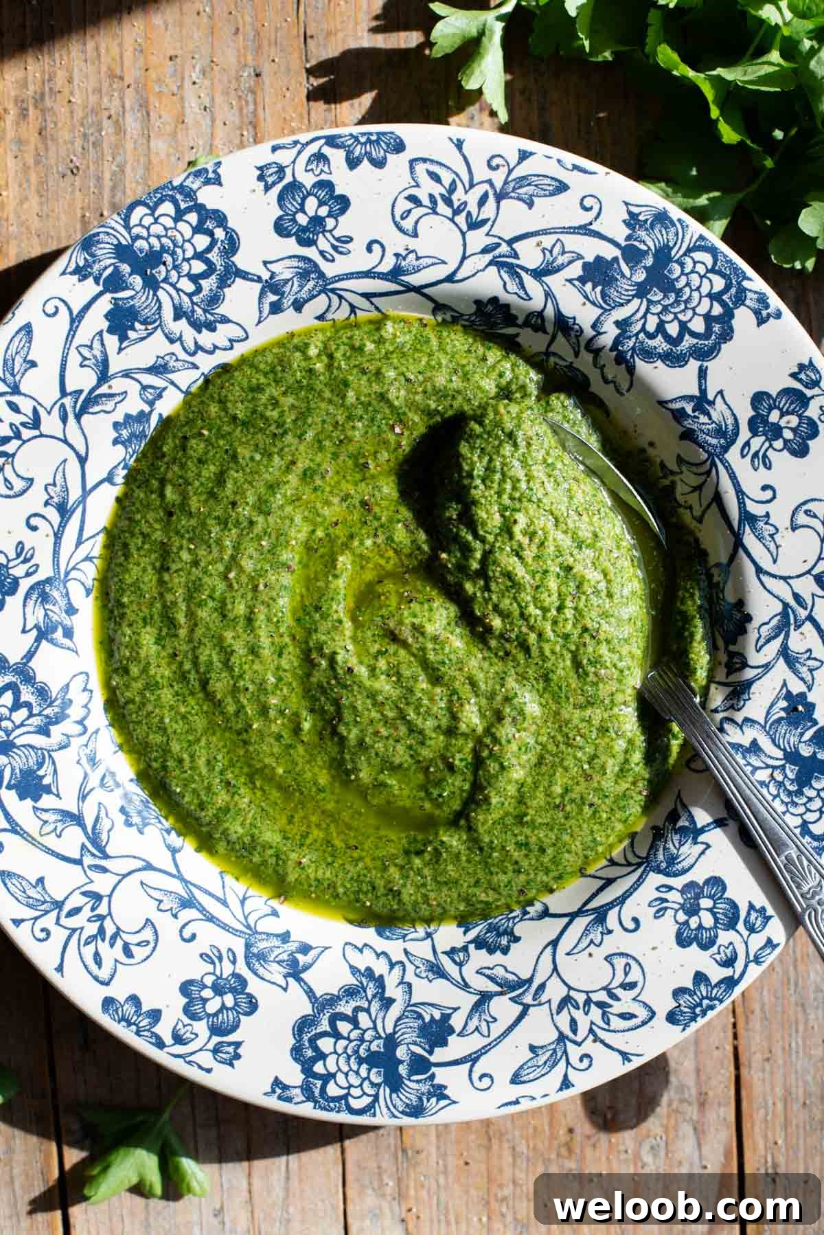 An overhead shot of a tuscan salsa verde in a blue and white bowl sitting on a wooden surface.
