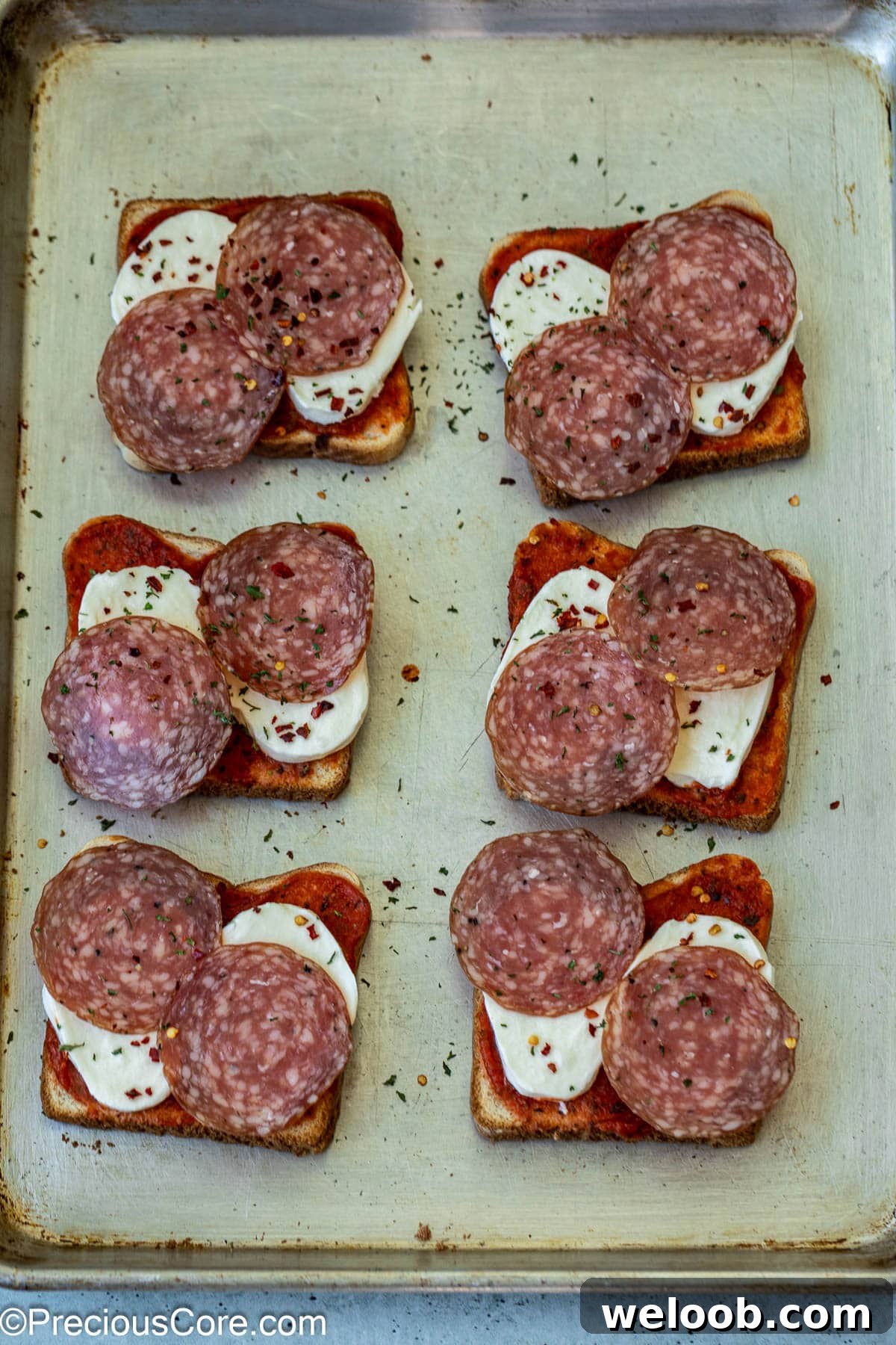 Salami with parsley flakes and pepper flakes sprinkled on unbaked pizza toasts.