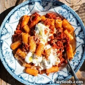 A close up of spicy calabrian sausage ragu in a blue and white bowl with stracciatella on top