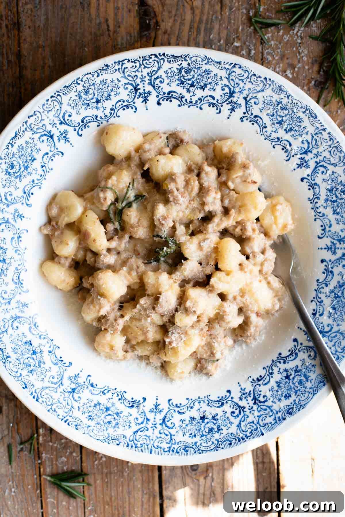 Creamy Sausage Ragu Gnocchi Recipe for Comfort Dinner 2 An overhead shot of gnocchi with a white creamy sausage ragu in a blue and white bowl on a rustic wooden surface.