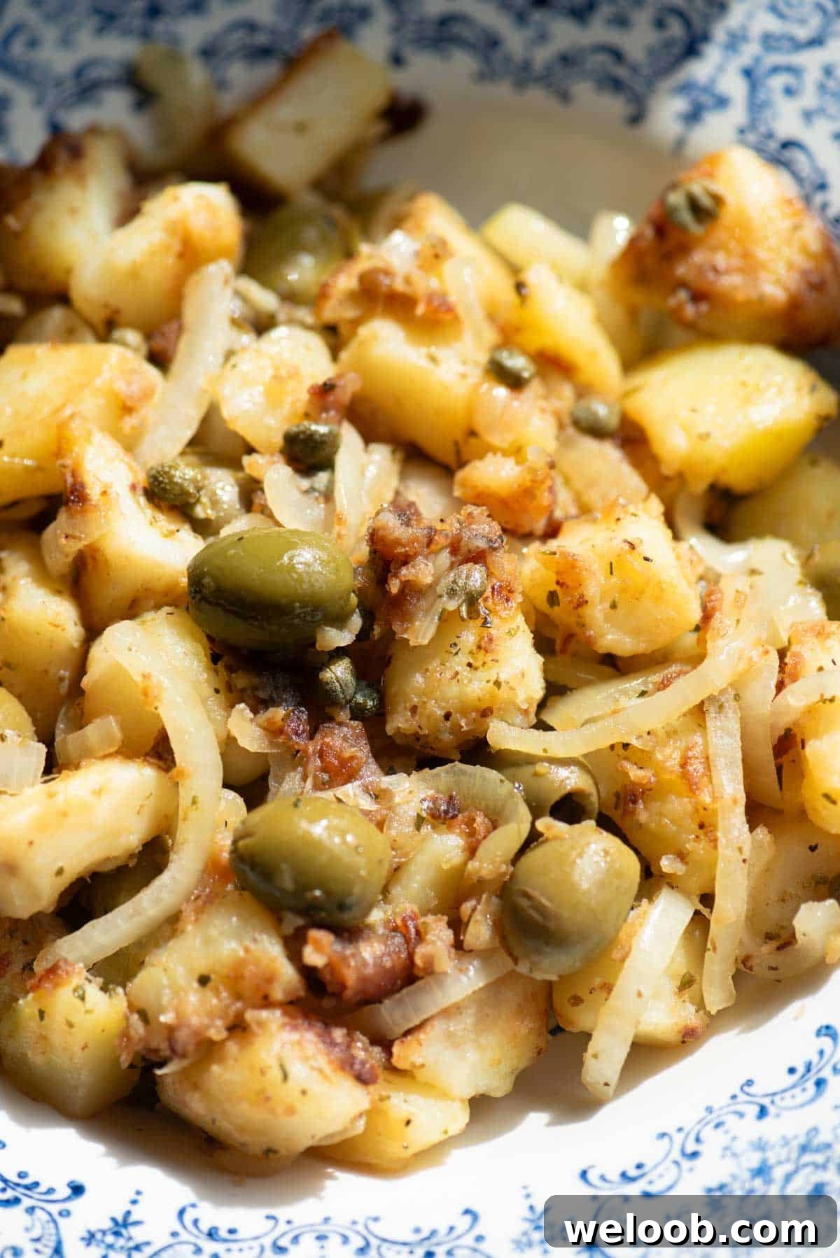 A close up of a potato side dish with olives, capers and oregano.