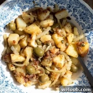 A close up of Sicilian potatoes in a blue bowl with capers and olives.