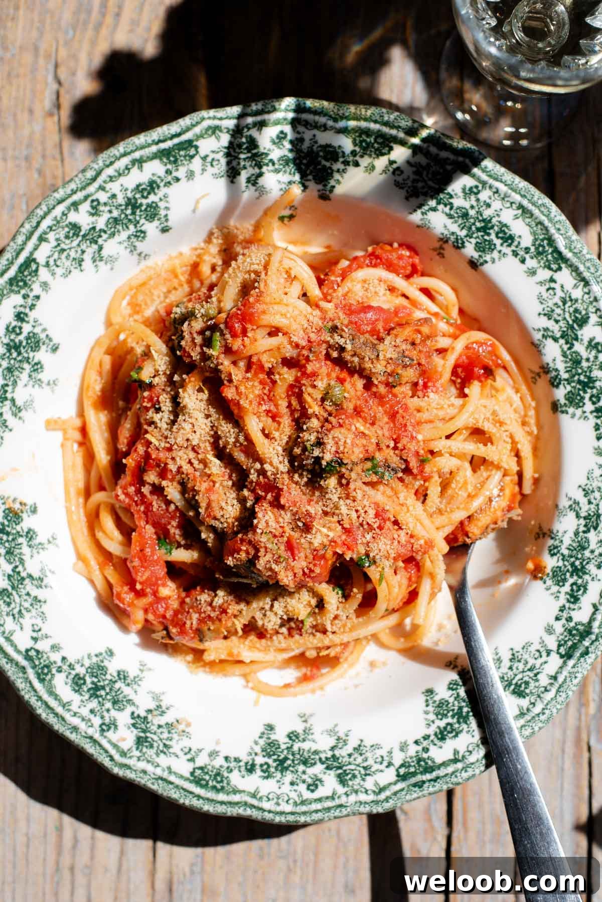 An overhead shot of spaghetti in a tomato sauce with sardines and breadcrumbs on top. The bowl is a vintage style green and white colour.