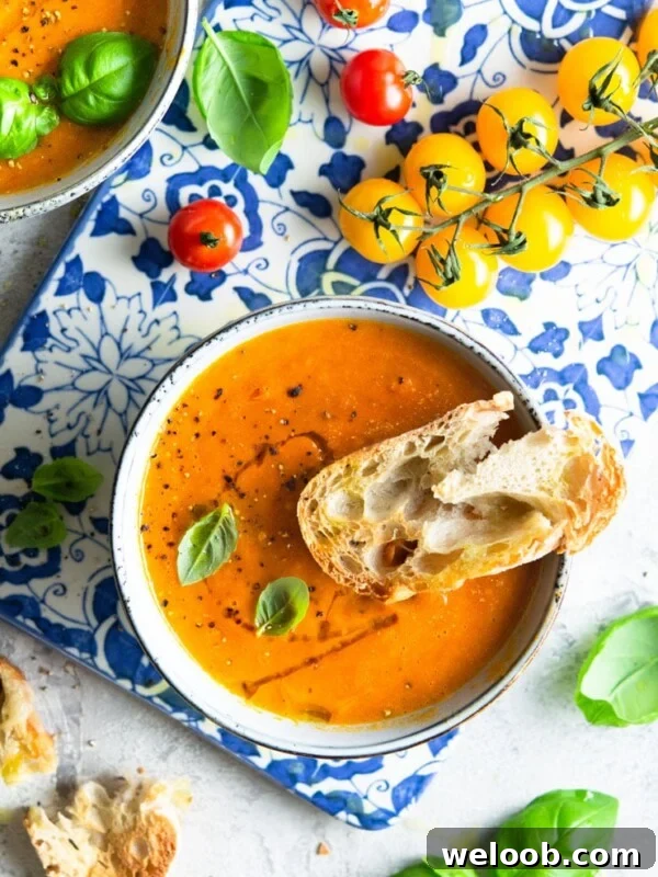 An overhead shot of roasted tomato soup with crusty bread a the side