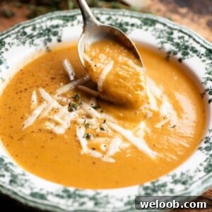 A close up of a spoon picking up some roasted vegetable soup from a green and white vintage style bowl.