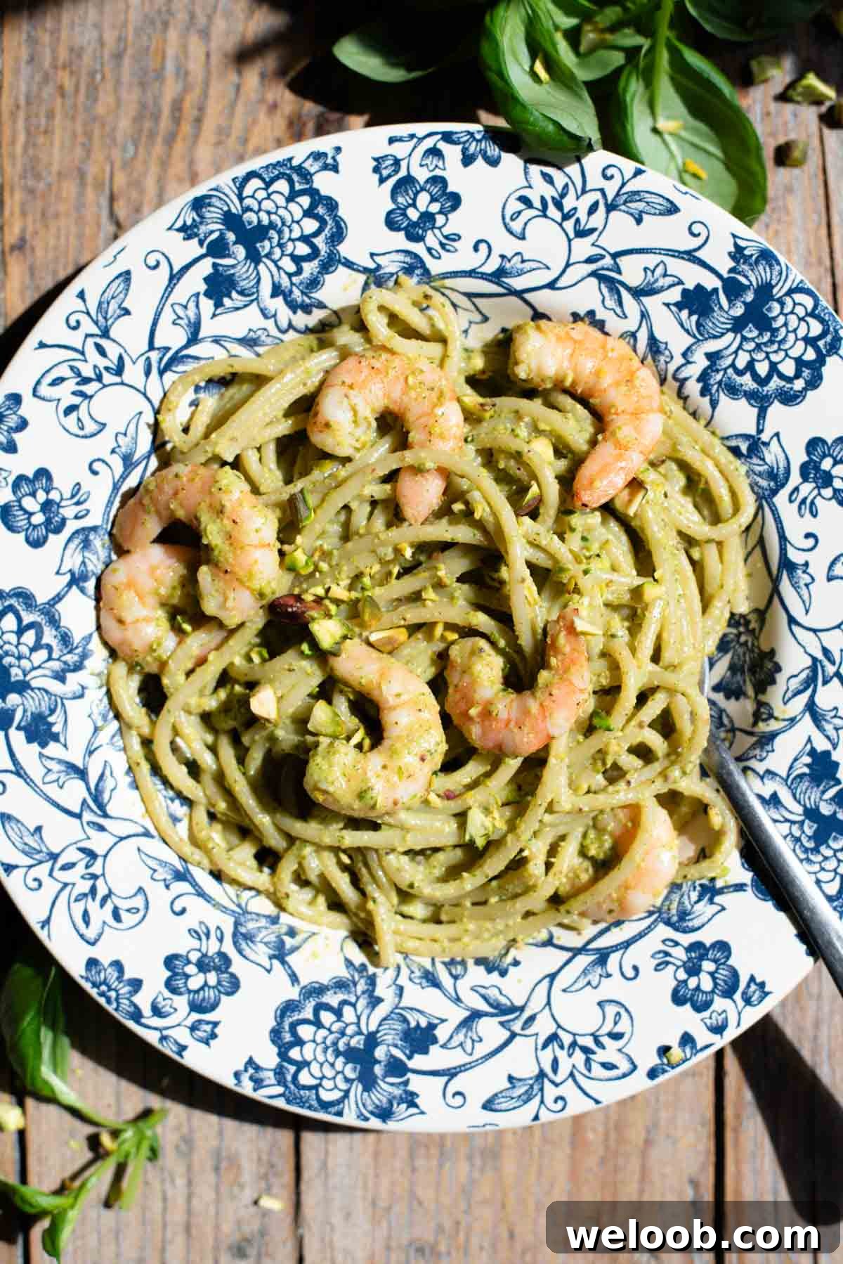 An overhead shot of pistachio pasta with shrimp in a blue floral bowl on a wooden background.