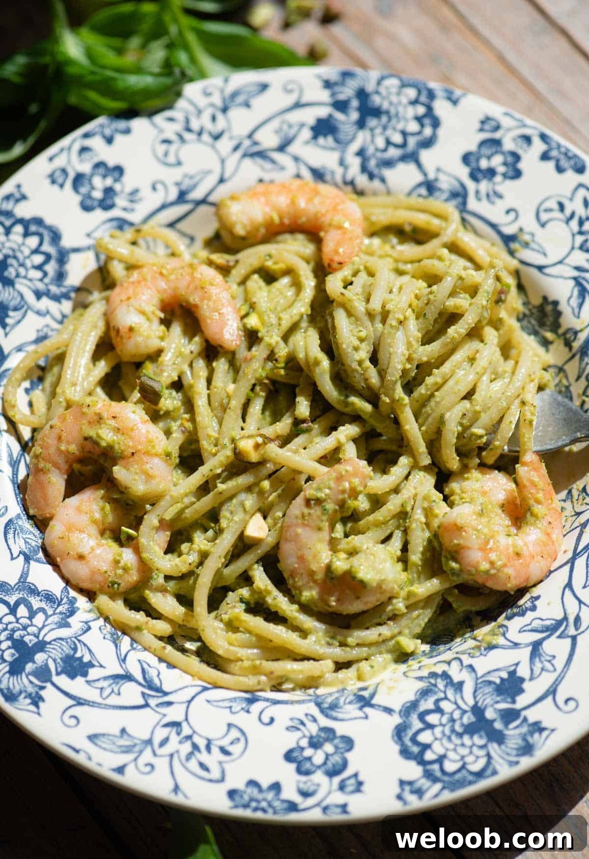 A side shot of pistachio shrimp spaghetti in a blue bowl sitting on a wooden background.