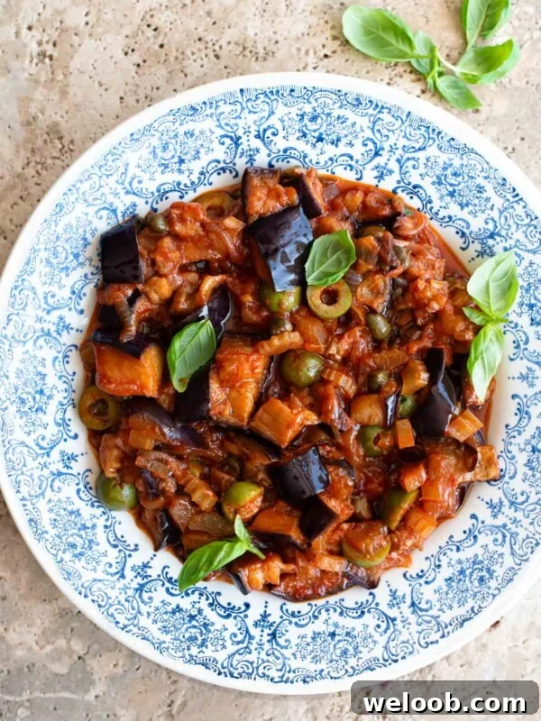 Sicilian caponata in a blue patterned bowl sitting on a travertine surface.