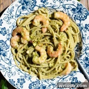 A close up of pistachio spaghetti with shrimps on a blue floral plate.