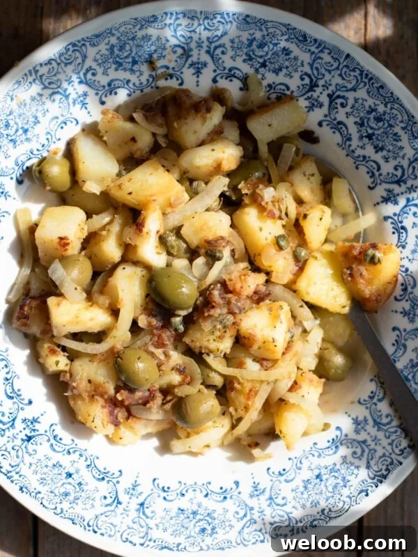 An overhead shot in direct sunlight of Sicilian potatoes in a blue bowl with olives and capers.