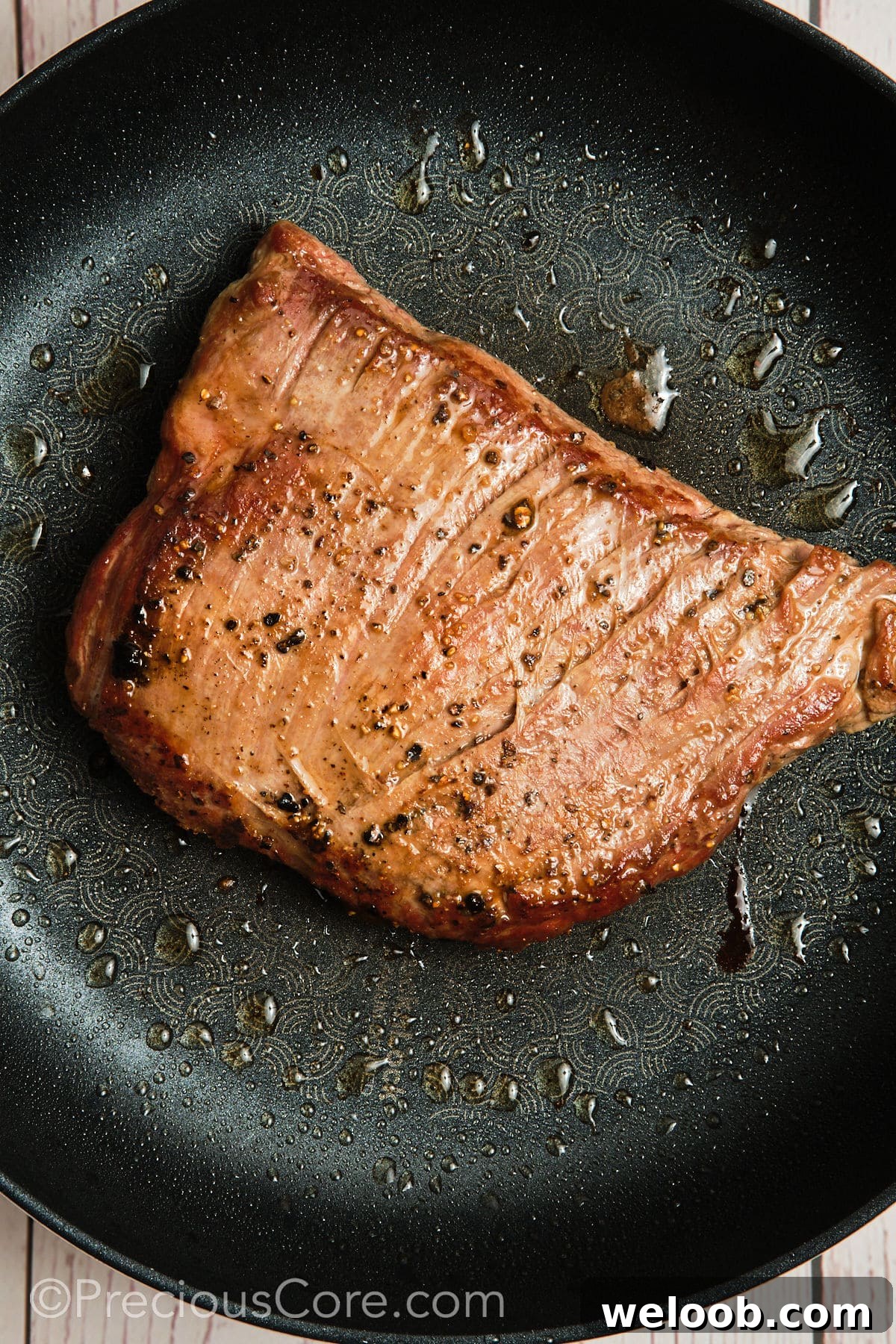 Searing a piece of flank steak in a hot skillet.