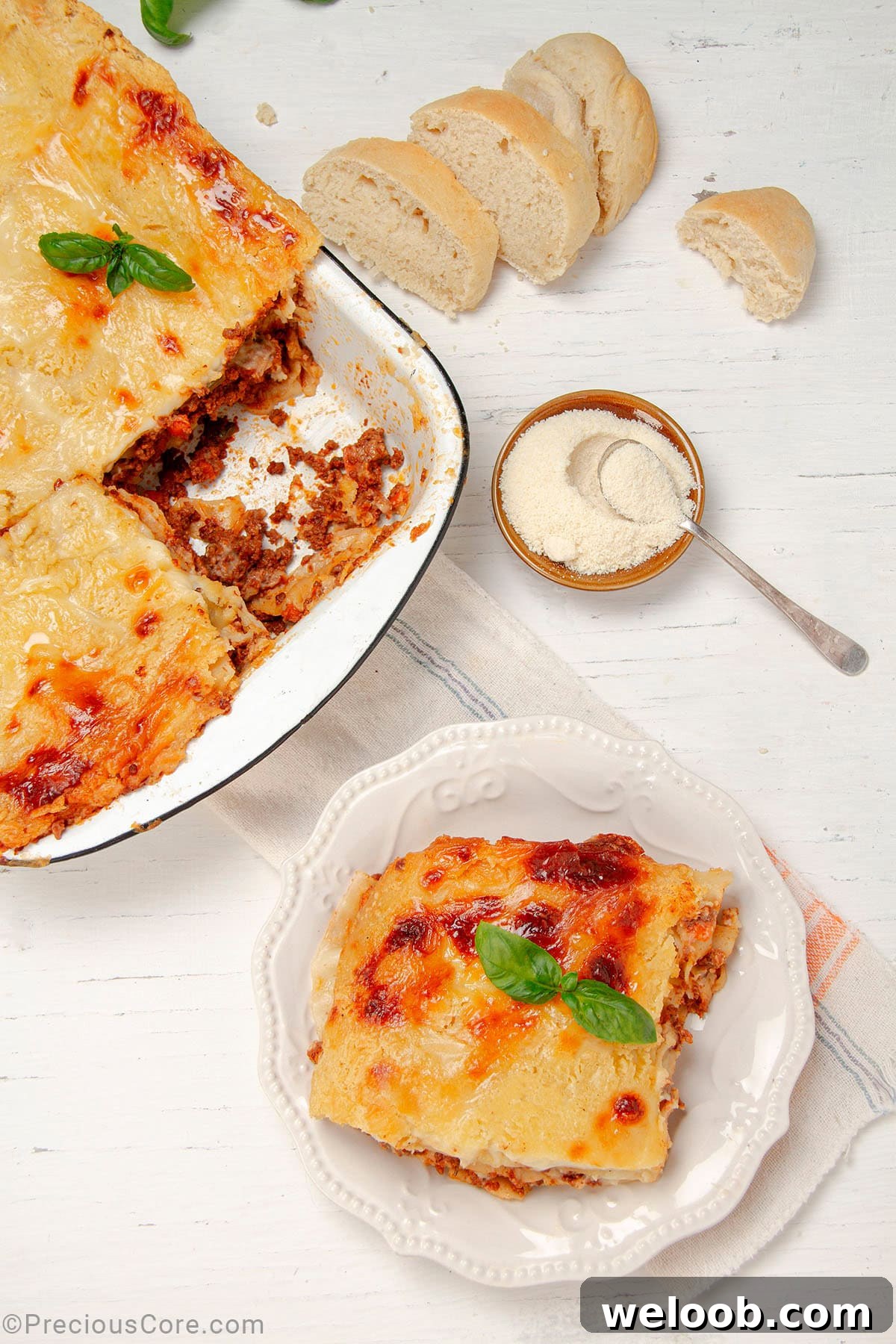 Slice of Lasagna on a plate with a bowl of freshly baked lasagna on the side.