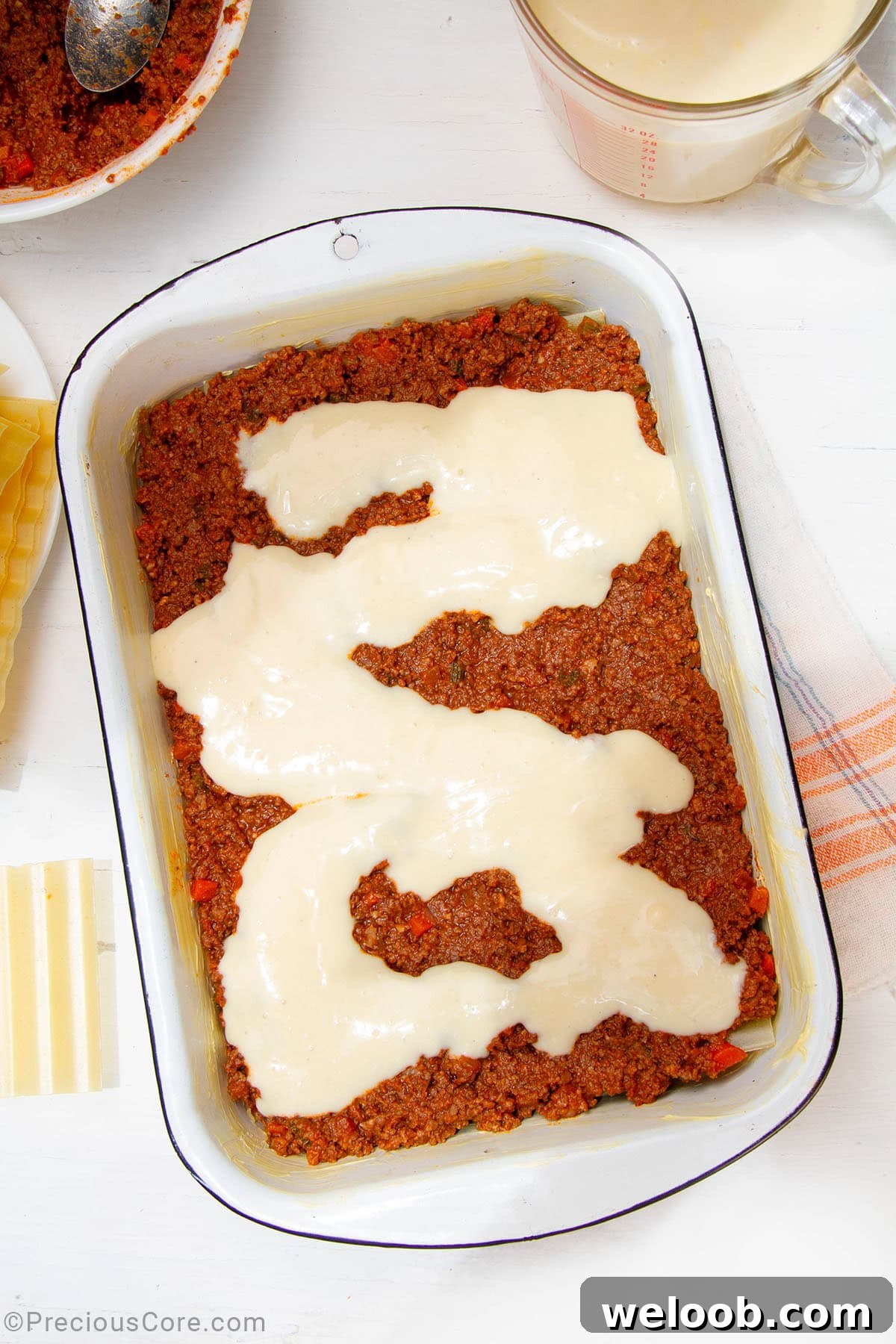 Béchamel sauce over meat sauce in a baking dish.