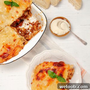 Slice of Lasagna on a plate with a bowl of freshly baked lasagna on the side.