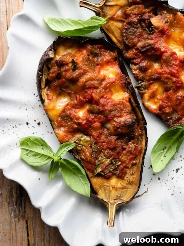Two stuffed eggplants on a scalloped edged plate with basil scattered around.