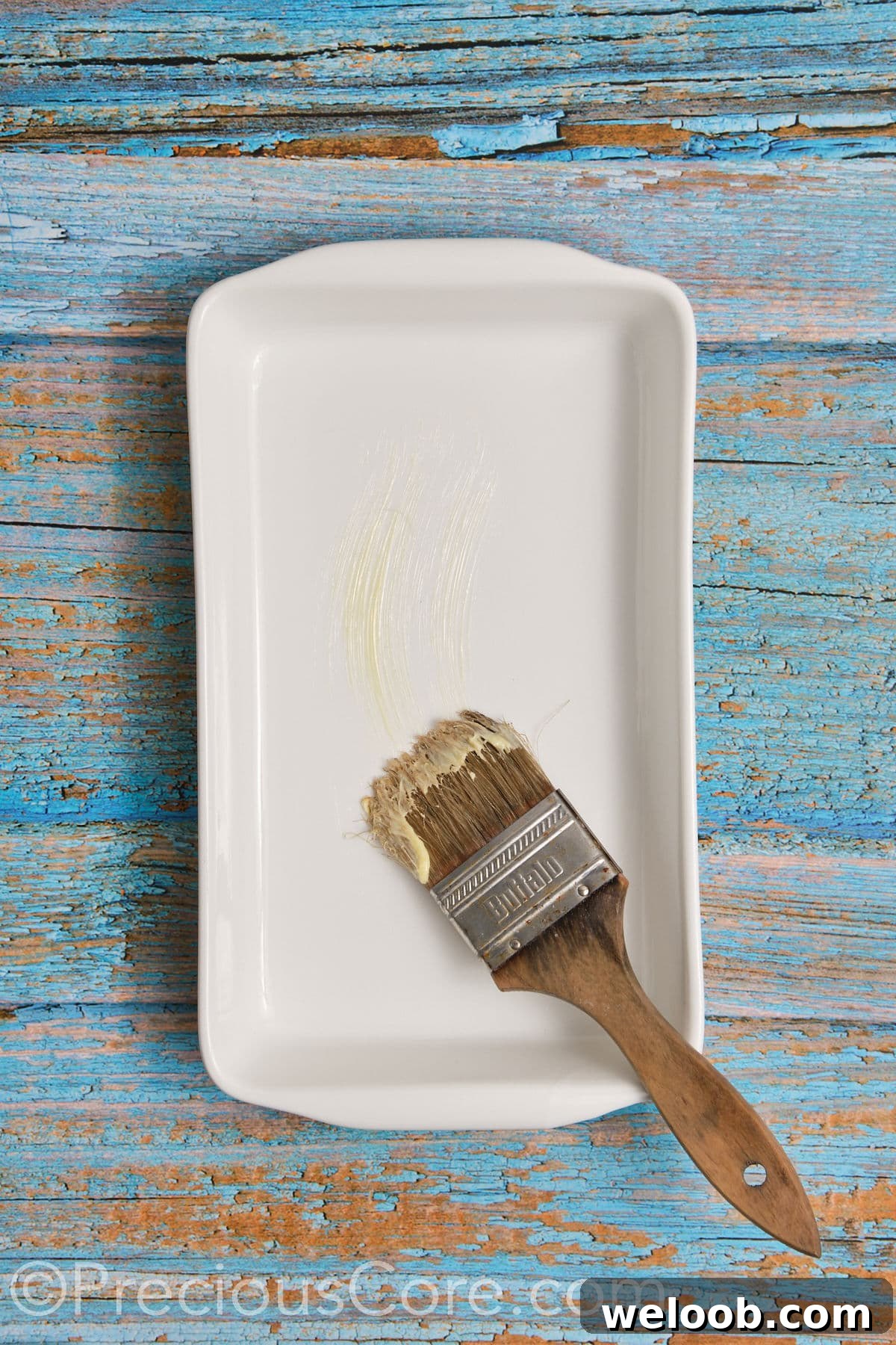 Brushing a casserole dish with softened butter.