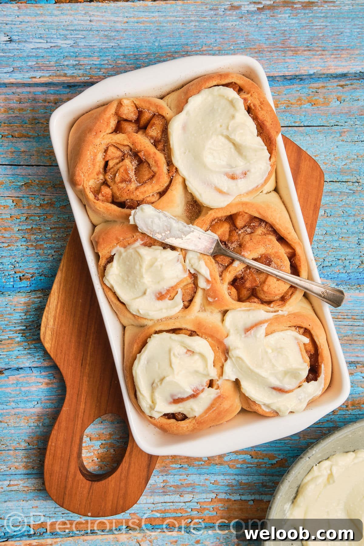 Spreading cream cheese frosting on apple cinnamon rolls.