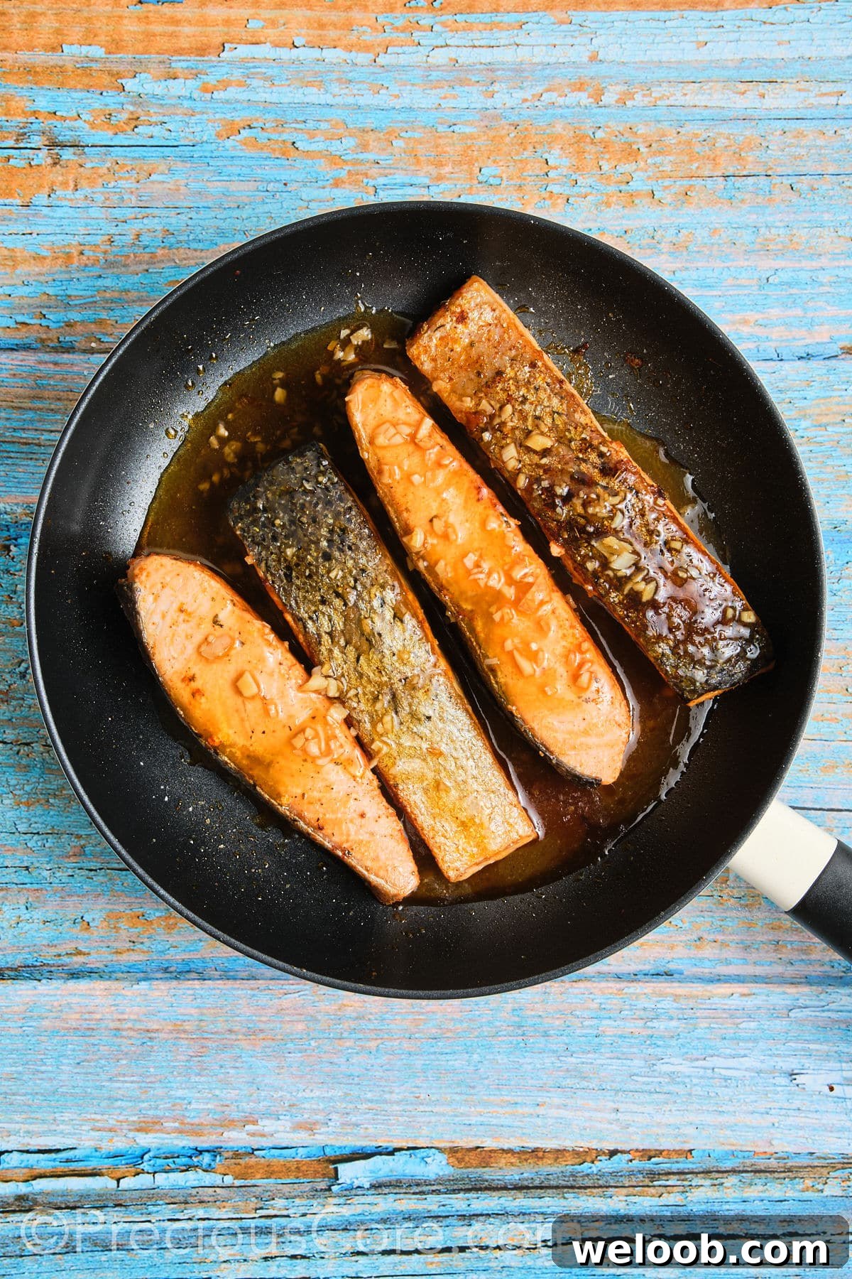 Salmon in skillet simmered in honey butter sauce.