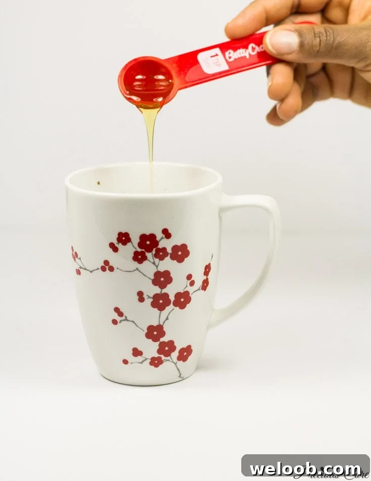Honey pouring into a floral mug.