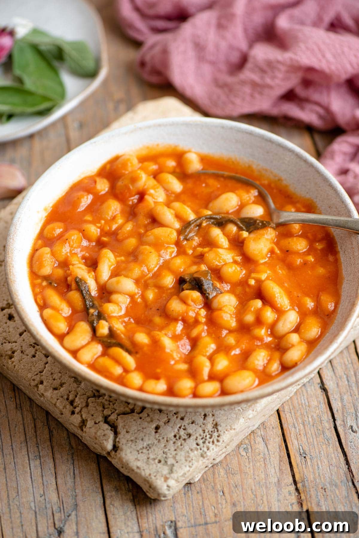 A bowl of cannellini bean in tomato sauce with sage sitting on a wooden surface