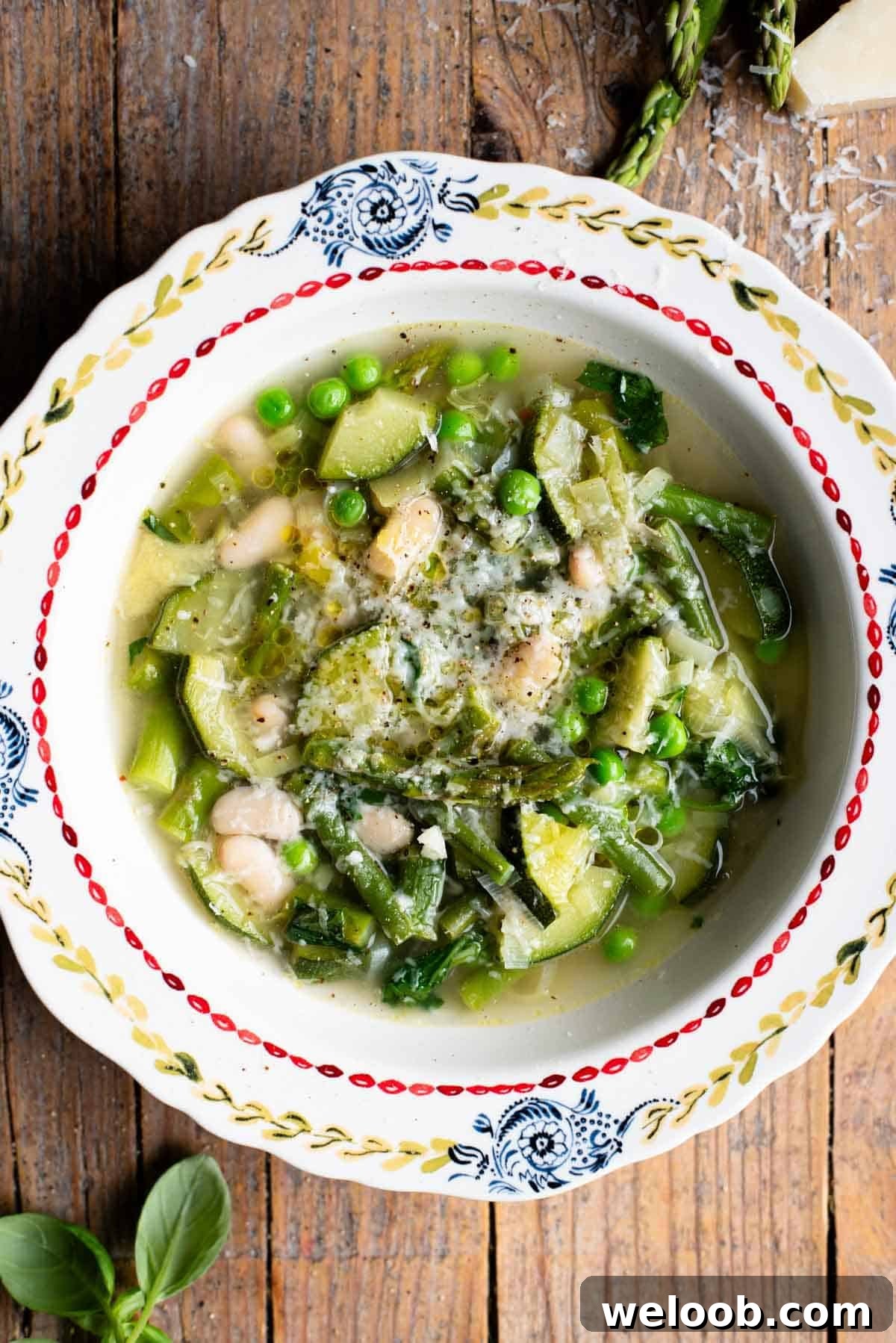 Spring soup, Minestrone Primavera with lots of green vegetables in a clear broth in a vintage patterned bowl on a wooden background.