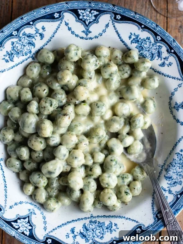 Mini spinach and potato gnocchi with a parmigiano and butter sauce in a blue and white bowl sitting on a wooden surface.